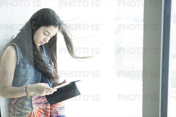 Hispanic girl using digital tablet at window
