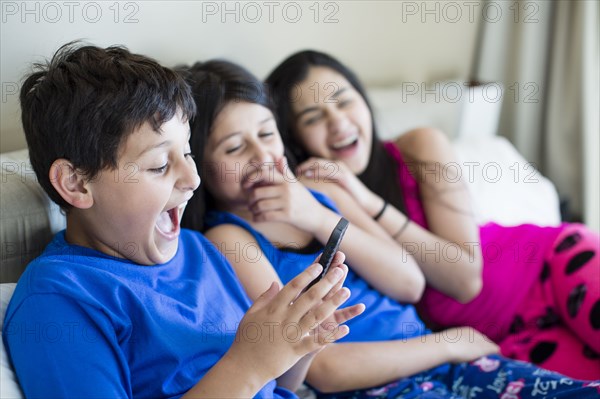 Hispanic siblings using cell phone on sofa