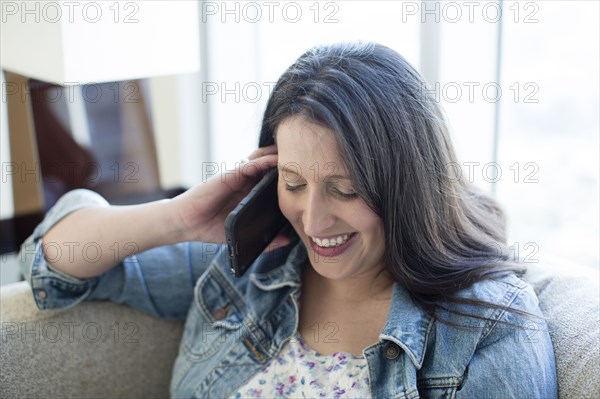 Hispanic woman talking on cell phone on sofa