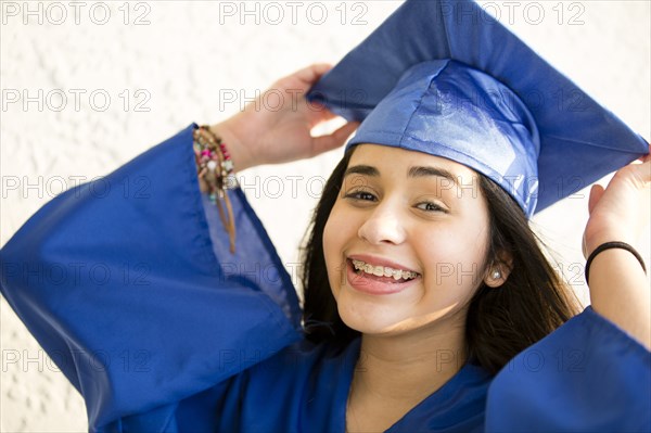 Smiling Hispanic girl wearing graduation robe and mortarboard