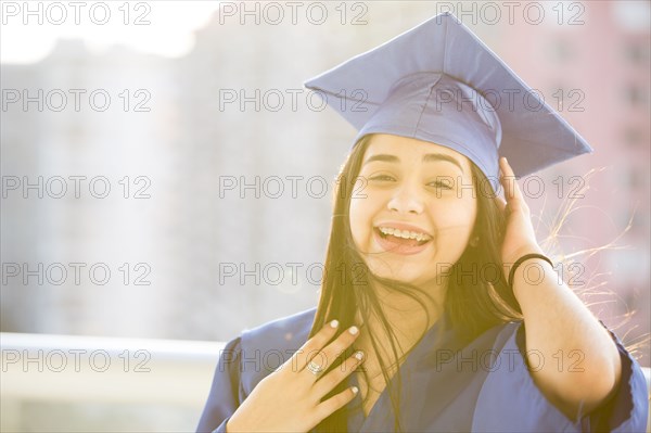 Smiling Hispanic girl wearing graduation robe and mortarboard