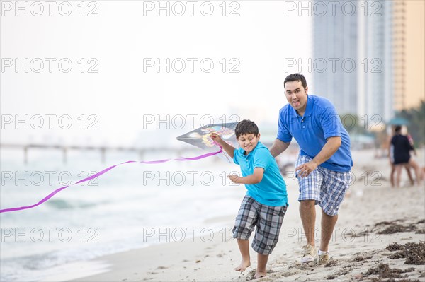 Hispanic father and son flying kite on beach