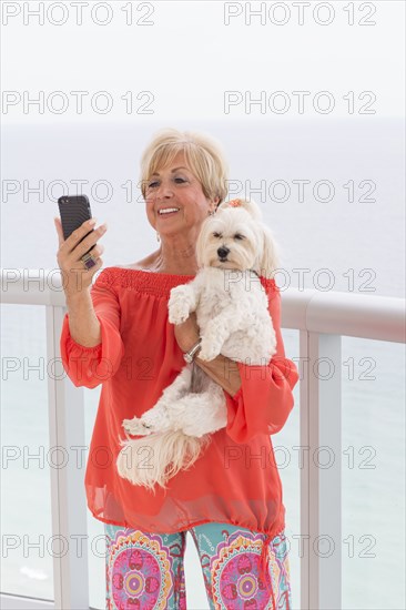 Older Caucasian woman taking selfie with dog on balcony
