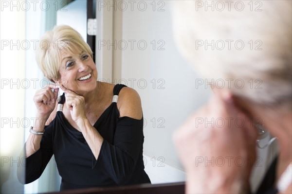 Older Caucasian woman attaching earring in mirror
