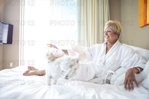 Older Caucasian woman petting dog on bed