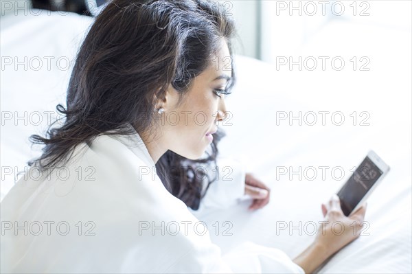 Hispanic woman using cell phone on bed