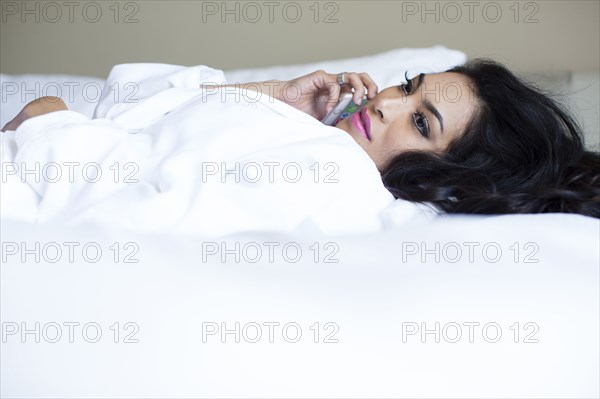 Hispanic woman talking on cell phone on bed