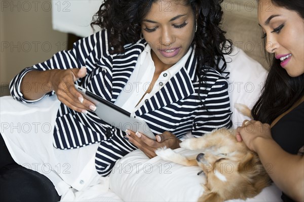 Close up of women petting dog and using digital tablet on bed