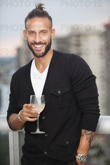 Hispanic man drinking wine on urban balcony