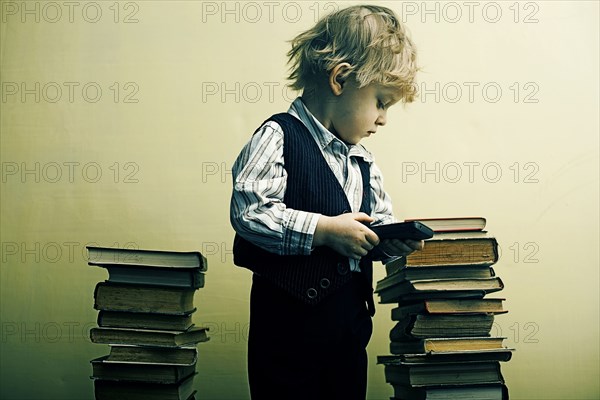 Boy holding cell phone near stacks of books