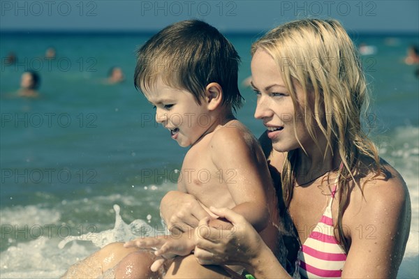 Wave splashing on mother holding son on beach