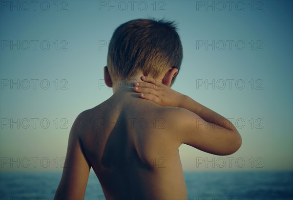 Boy rubbing neck at beach