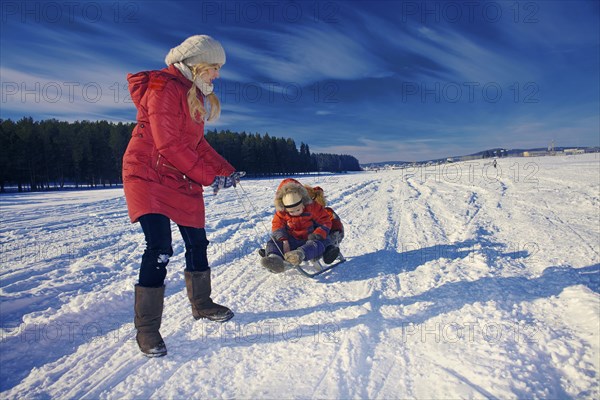 Mother and sons sledding in snowy remote field