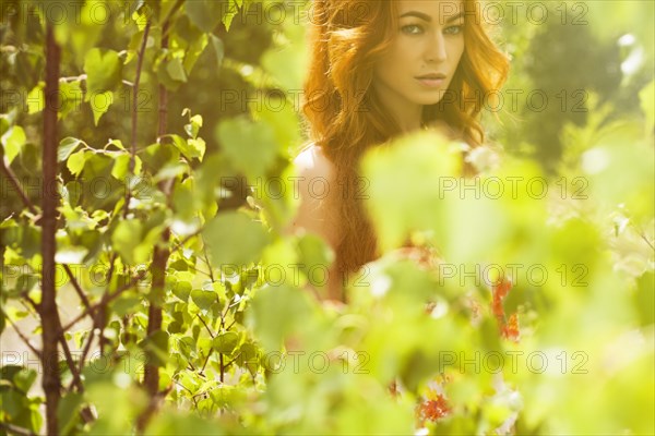 Caucasian woman posing behind foliage