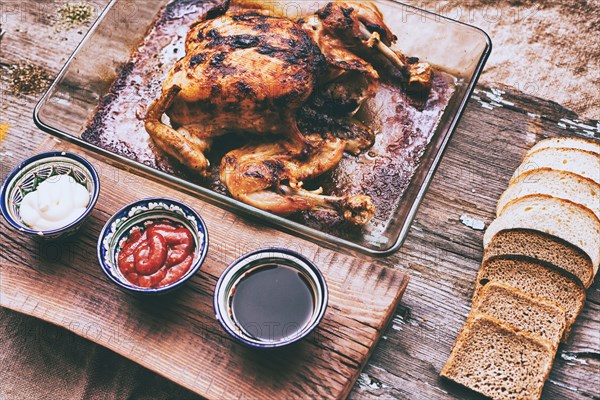 Close up of roasted chicken with bread and sauces on wooden table