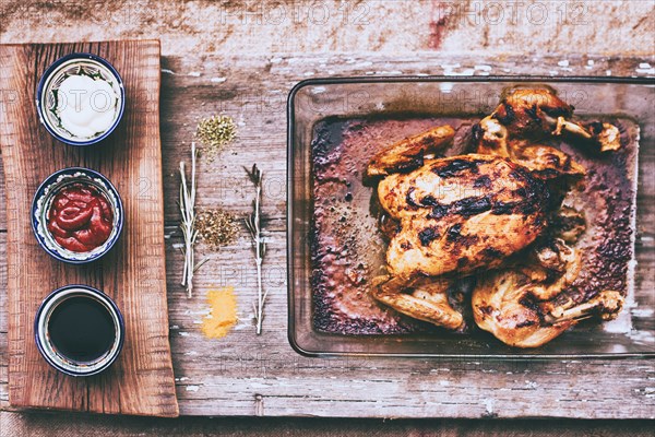 Close up of roasted chicken with rosemary and sauces on wooden table