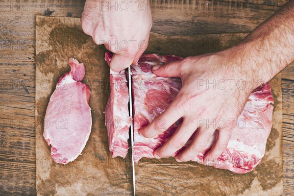 Hands of man cutting raw meat on butcher paper with knife