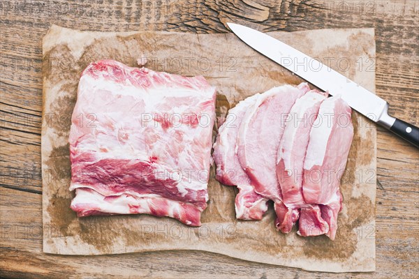 Slices of raw meat on butcher paper near knife