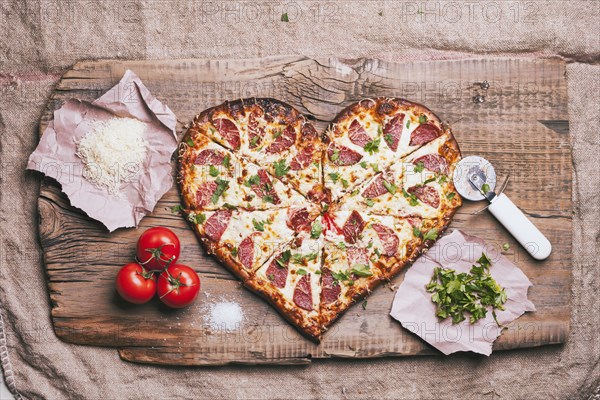 Heart-shaped pizza and ingredients on cutting board