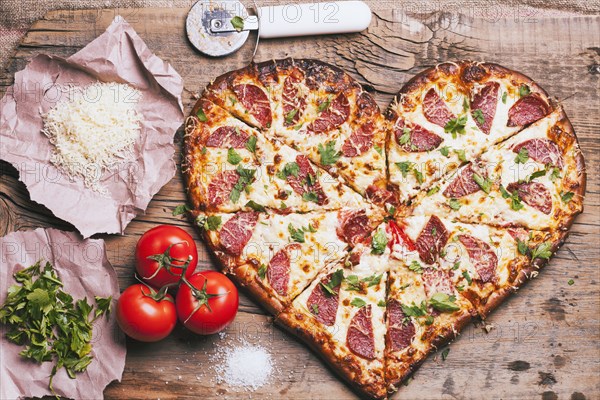 Heart-shaped pizza and ingredients on cutting board