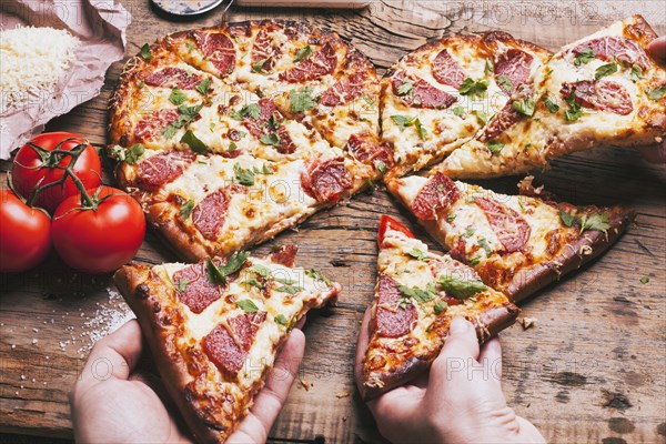 Hands pulling slices of heart-shaped pizza near ingredients on cutting board