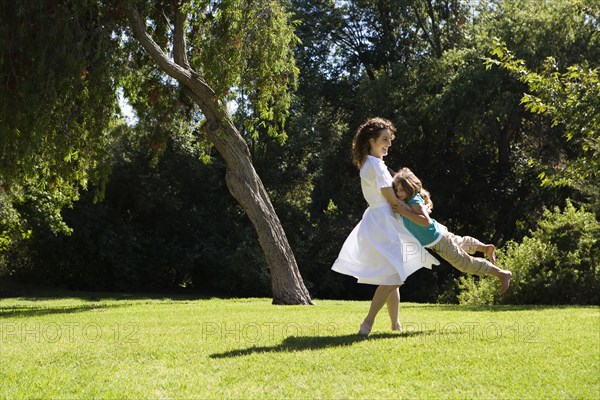 Mother swinging daughter in park