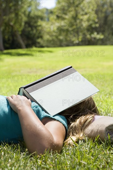 Girl sleeping in grass with book on her head