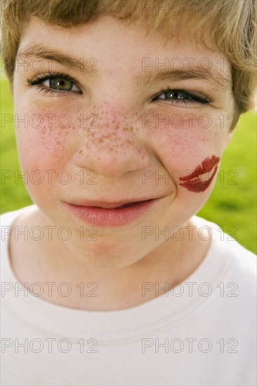 Grimacing boy with lipstick kiss on face