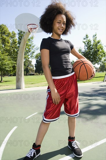 Smiling teenage girl holding basketball on court