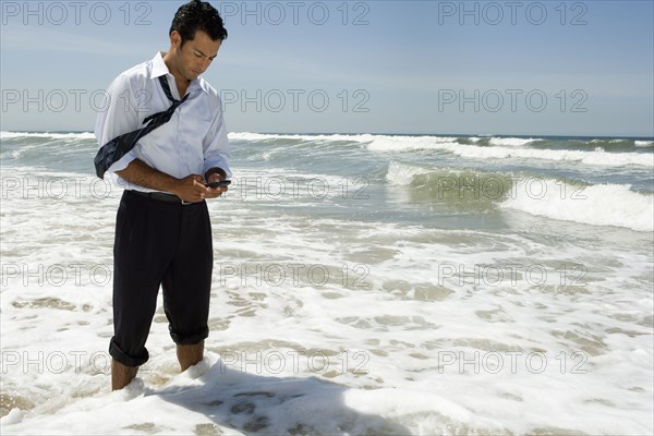 Businessman text messaging on cell phone while standing in ocean