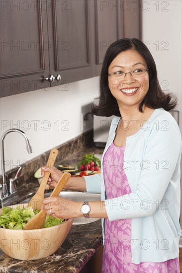 Chinese woman tossing salad in kitchen