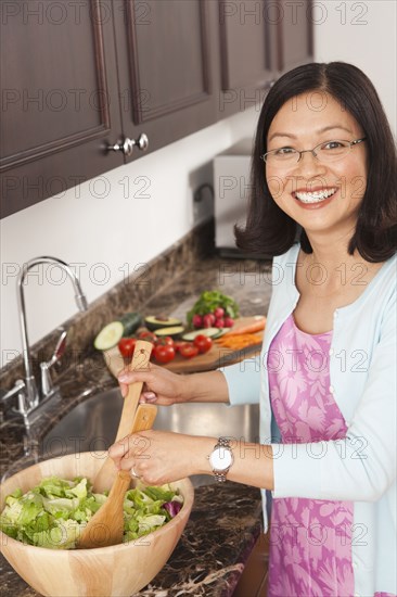 Chinese woman tossing salad in kitchen