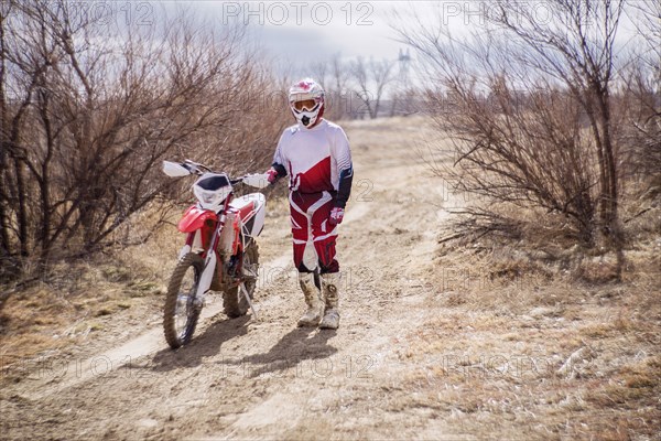 Dirt bike rider standing with motorcycle in rural field