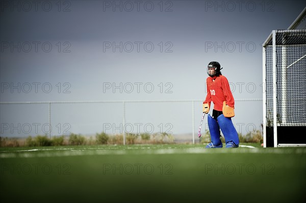 Mixed race field hockey goalie standing by goal