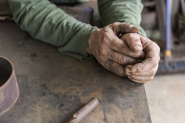 Rugged hands of artist leaning on table in workshop