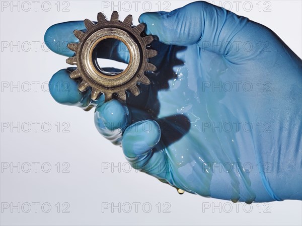 Hand wearing rubber-glove holding gear dripping with oil