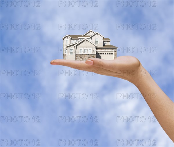 Hand of woman holding house in sky