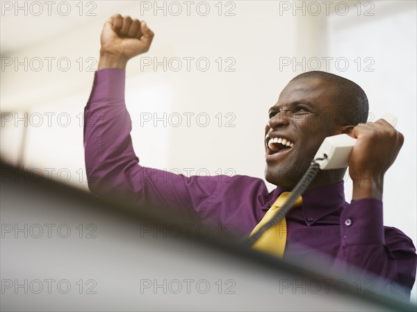 Cheering Black businessman holding telephone