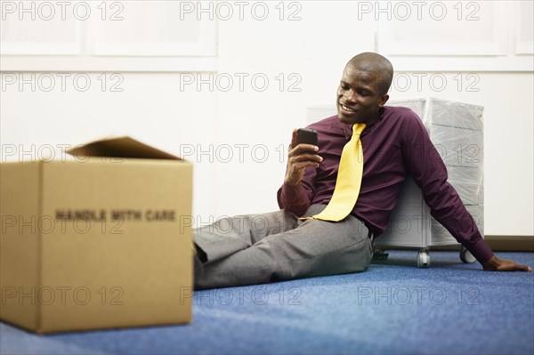 Black businessman sitting on floor text messaging