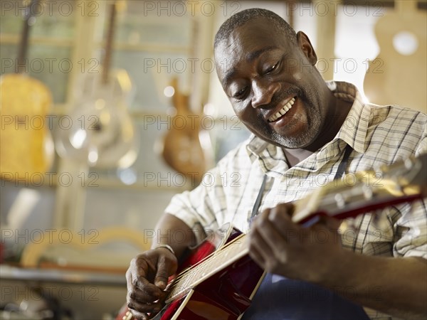 Black craftsman playing guitar in workshop