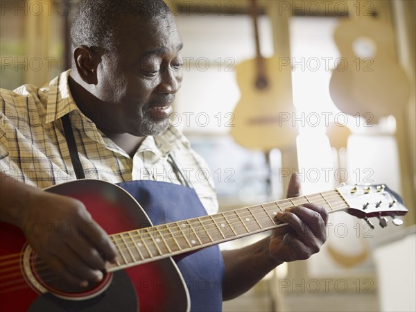 Black craftsman playing guitar in workshop