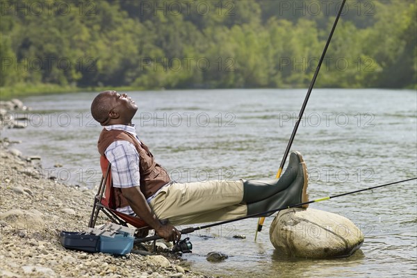 Black man with feet up fishing in stream