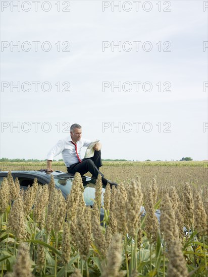 Caucasian businessman sitting on top of car in field