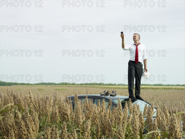 Caucasian businessman on top of car in field looking at gps device