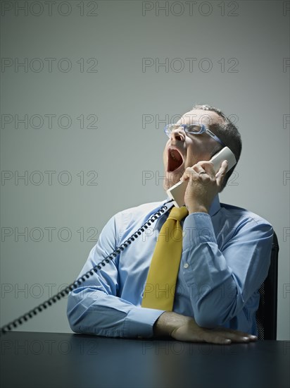 Caucasian businessman yawning and talking on telephone