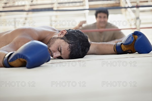 Knocked-out Hispanic boxer laying on ground