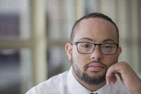Mixed race man with down syndrome resting chin in hands