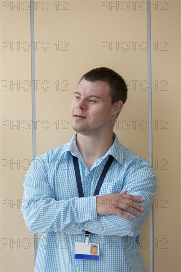 Caucasian man with Down Syndrome wearing badge at wall