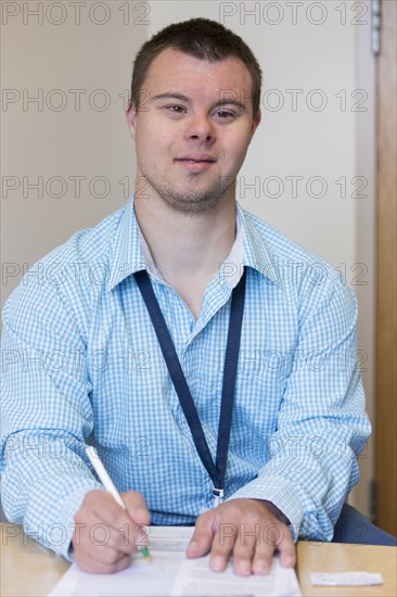 Caucasian man with Down Syndrome writing notes at desk