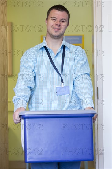 Caucasian man with Down Syndrome carrying bin in office